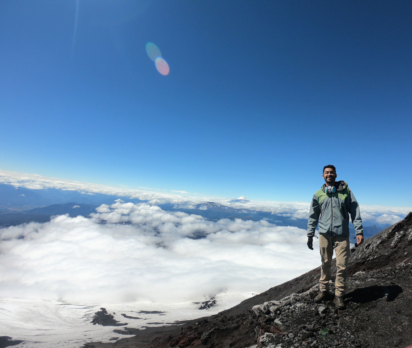 Ricardo standing on the top of a mountain with a beautiful landscape and clouds behind him