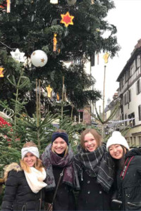 Tracie with three friends smiling in front of a decorated Christmas tree