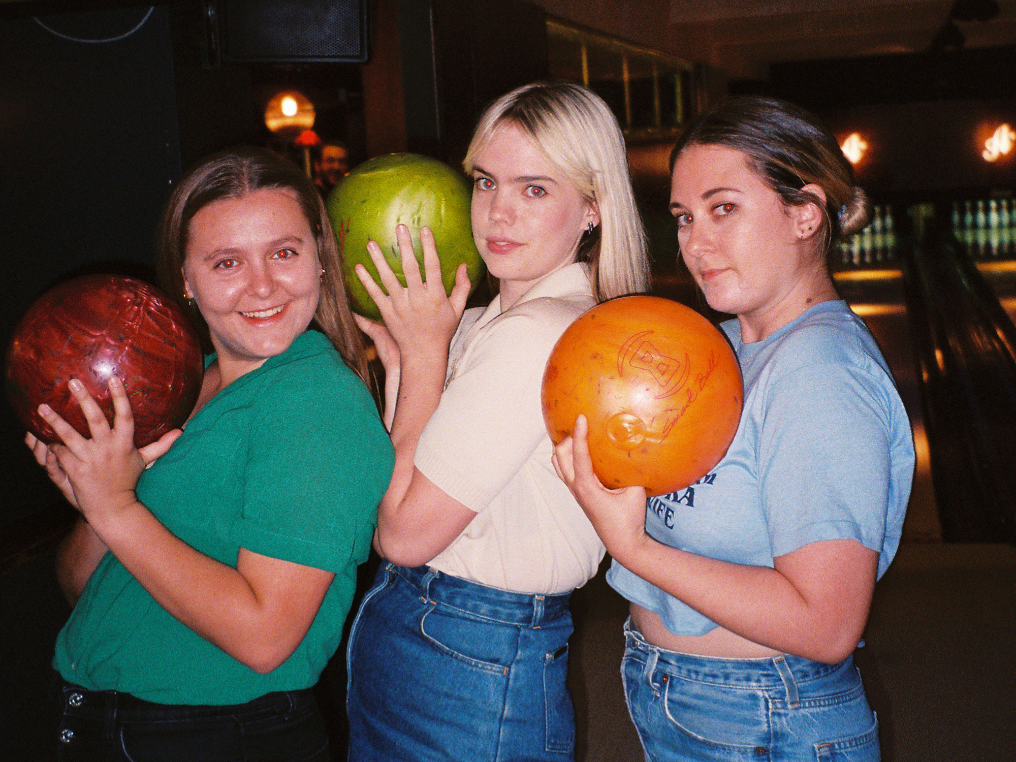 Three friends smiling and holding bowling balls 