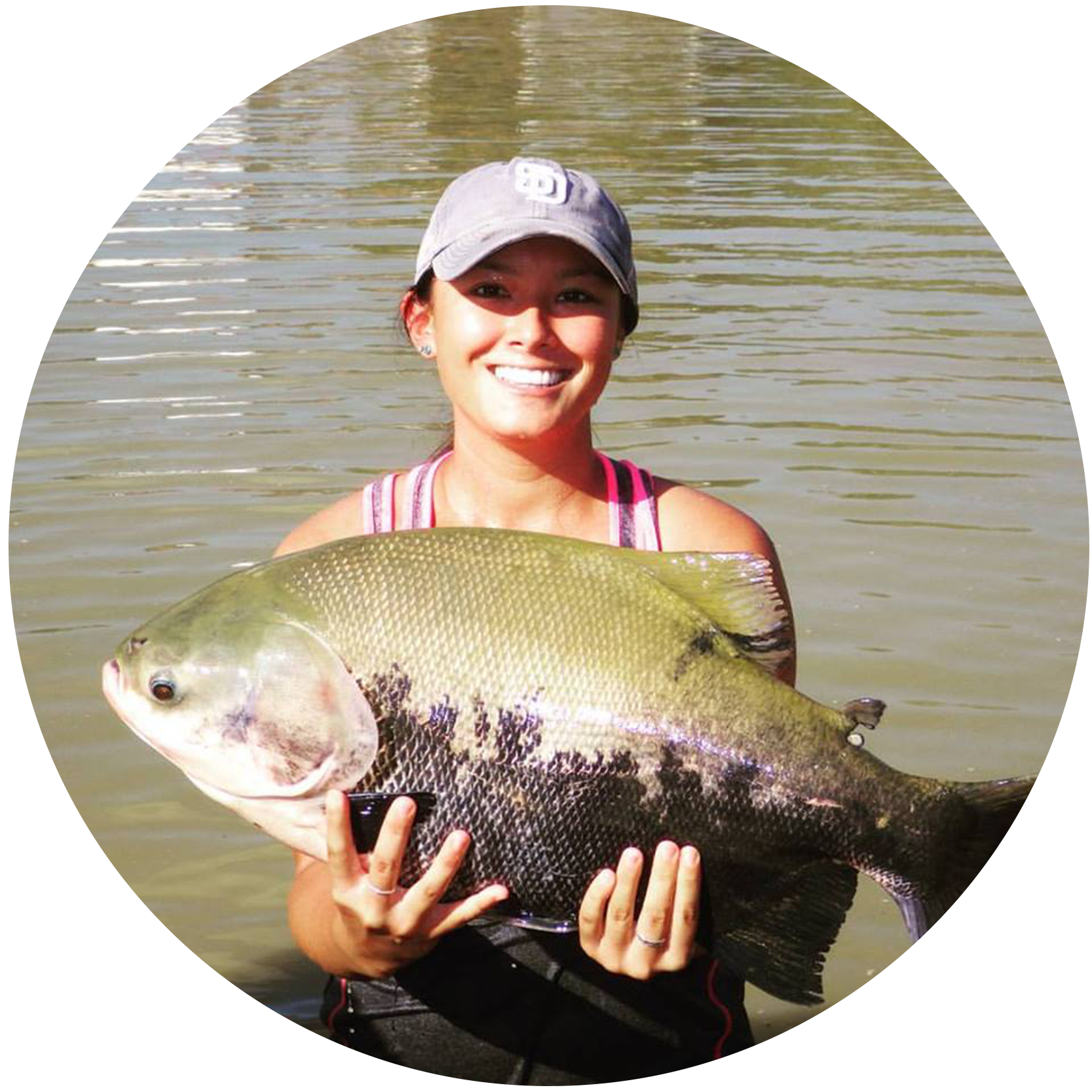 Rachel Shinto holds up a fish in front of a body of a water.