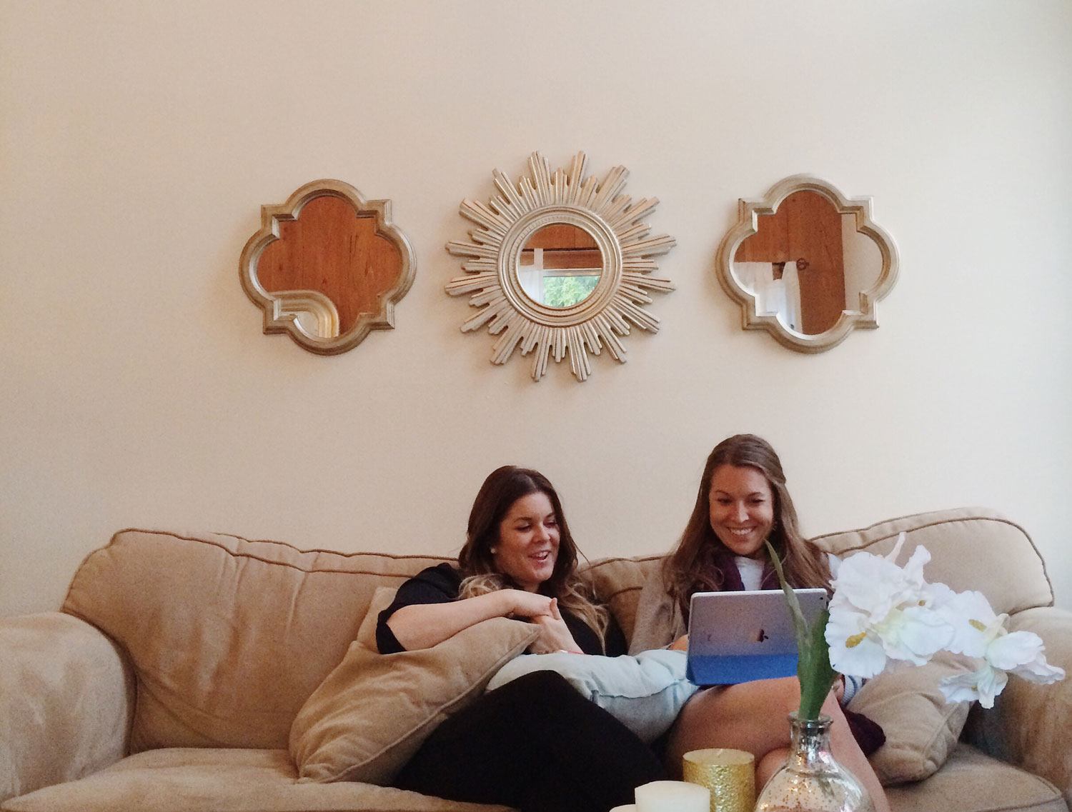 Two friends sitting on a couch, looking at a laptop together and smiling