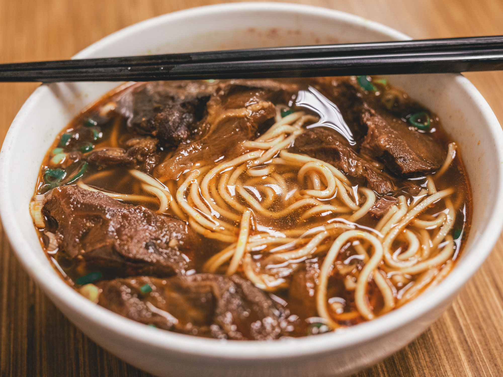 Beef and noodles with chopsticks in a white bowl.