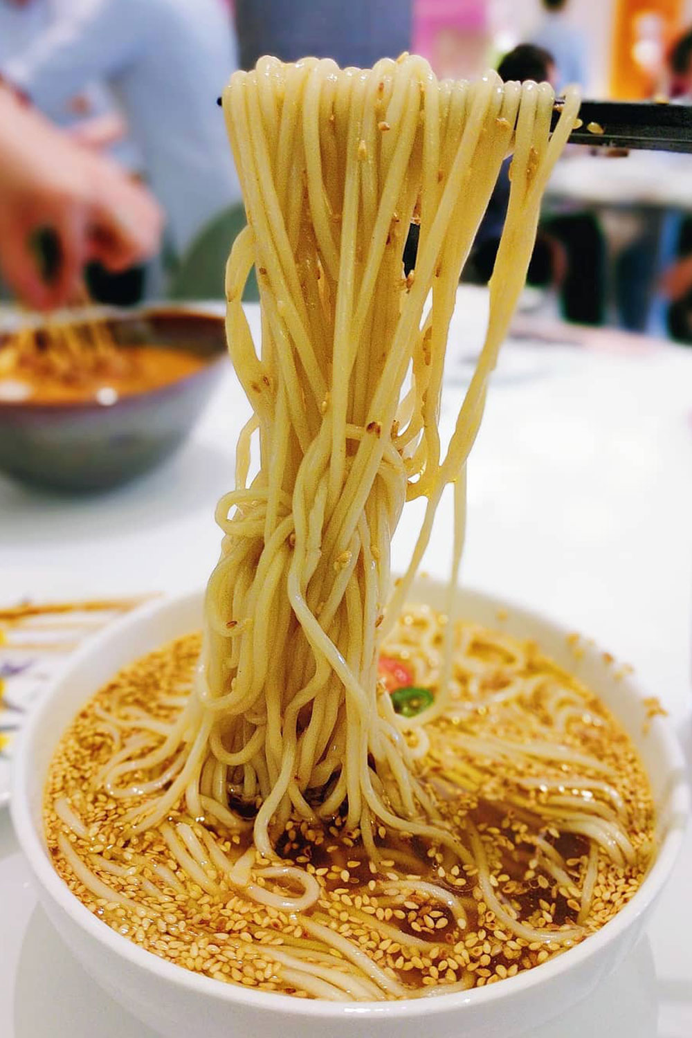 A noodle soup dish with noodles hanging from chopsticks.