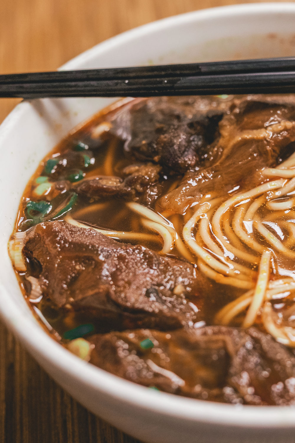 Beef and noodles with chopsticks in a white bowl.