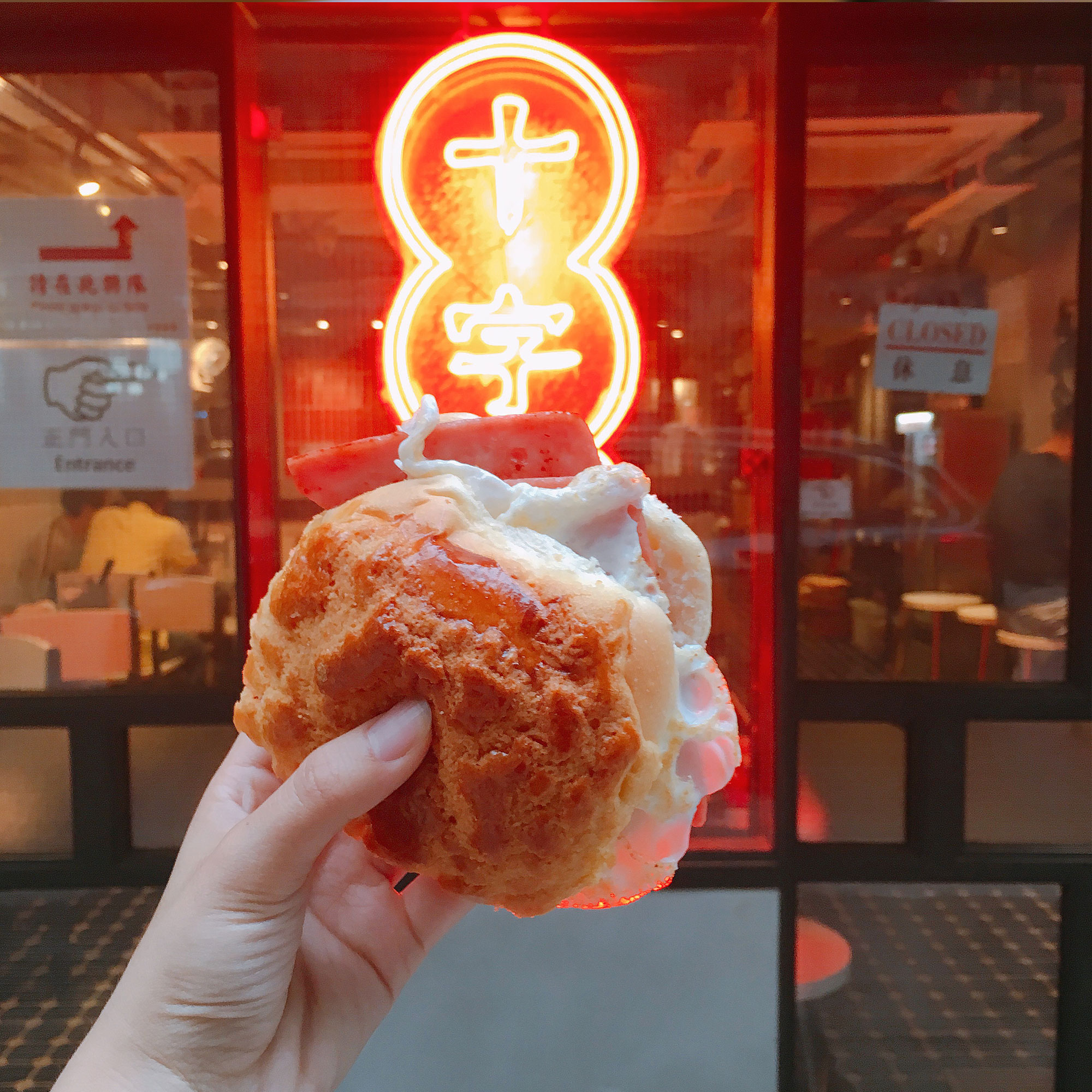 Student holding a Ham and Egg Pineapple Bun with a neon sign in the background.