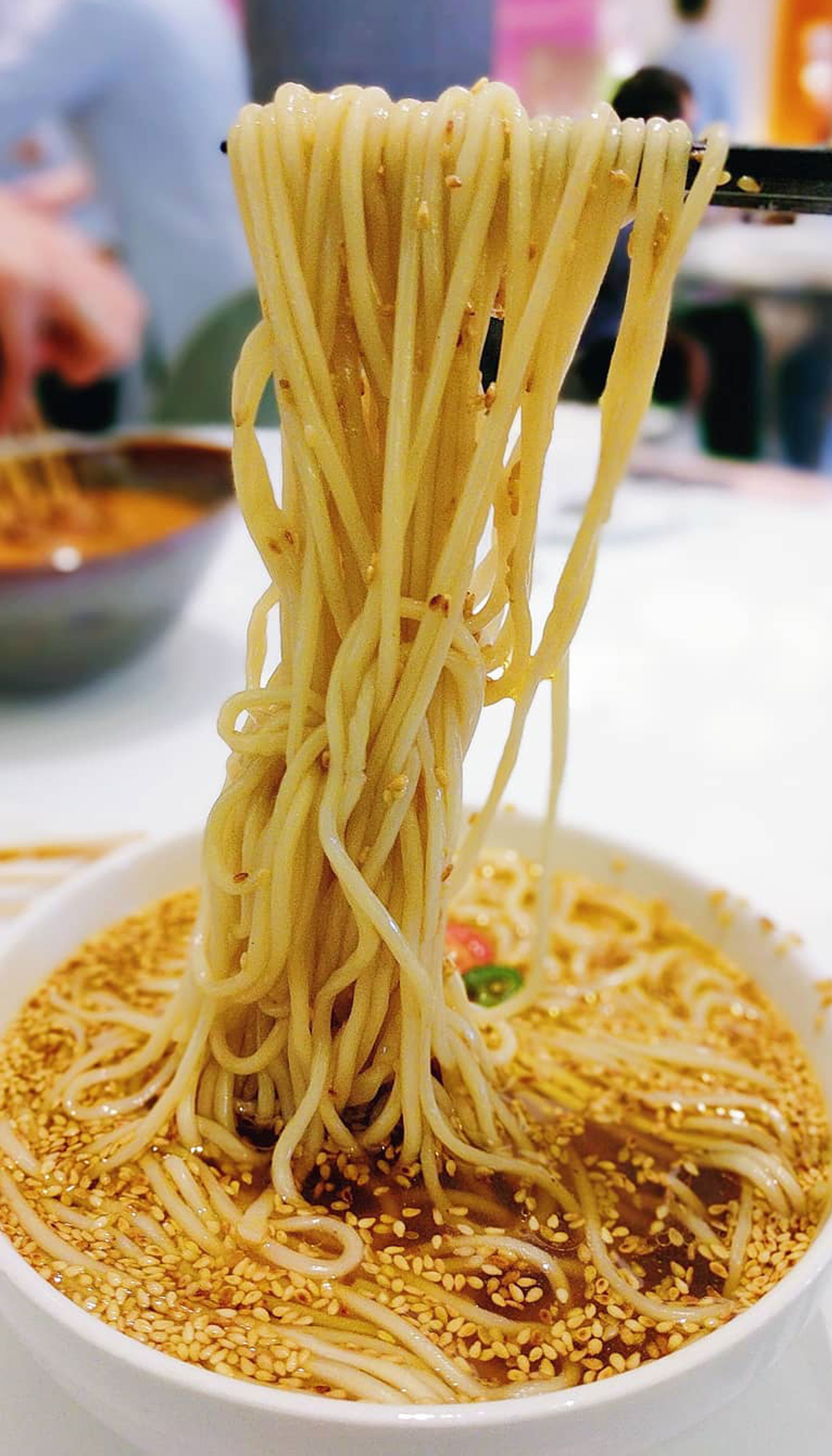 A noodle soup dish with noodles hanging from chopsticks.