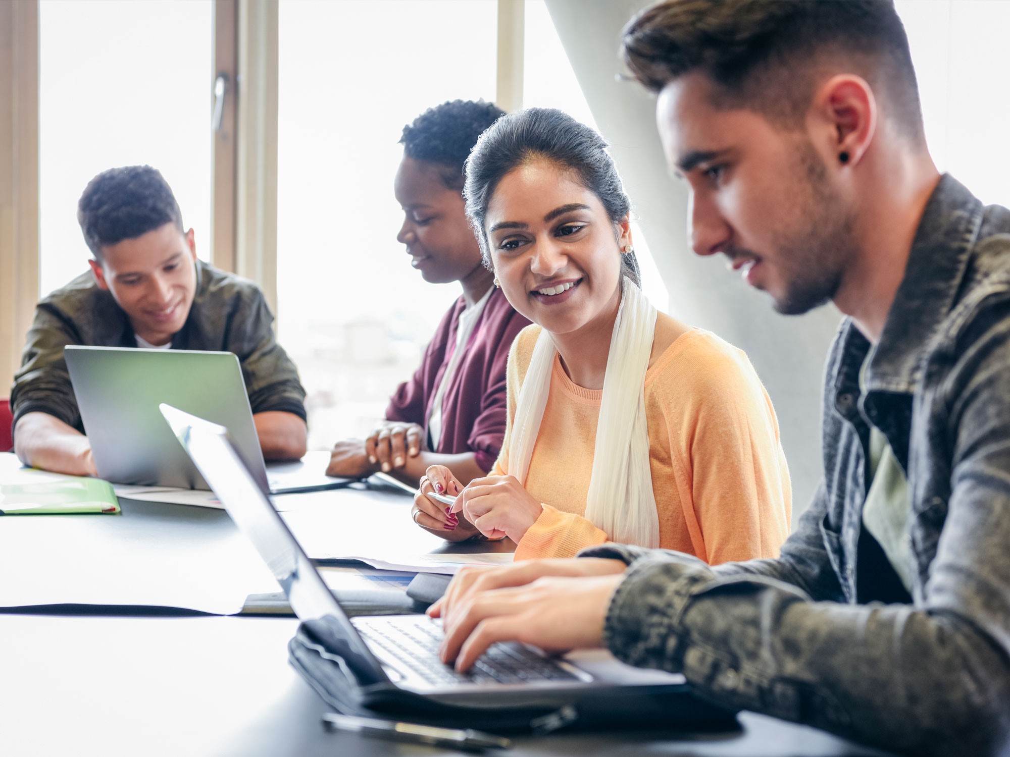 Young man using laptop with female student watching and smiling