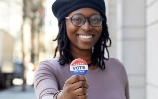 Portrait of smiling woman showing Vote button in a city.