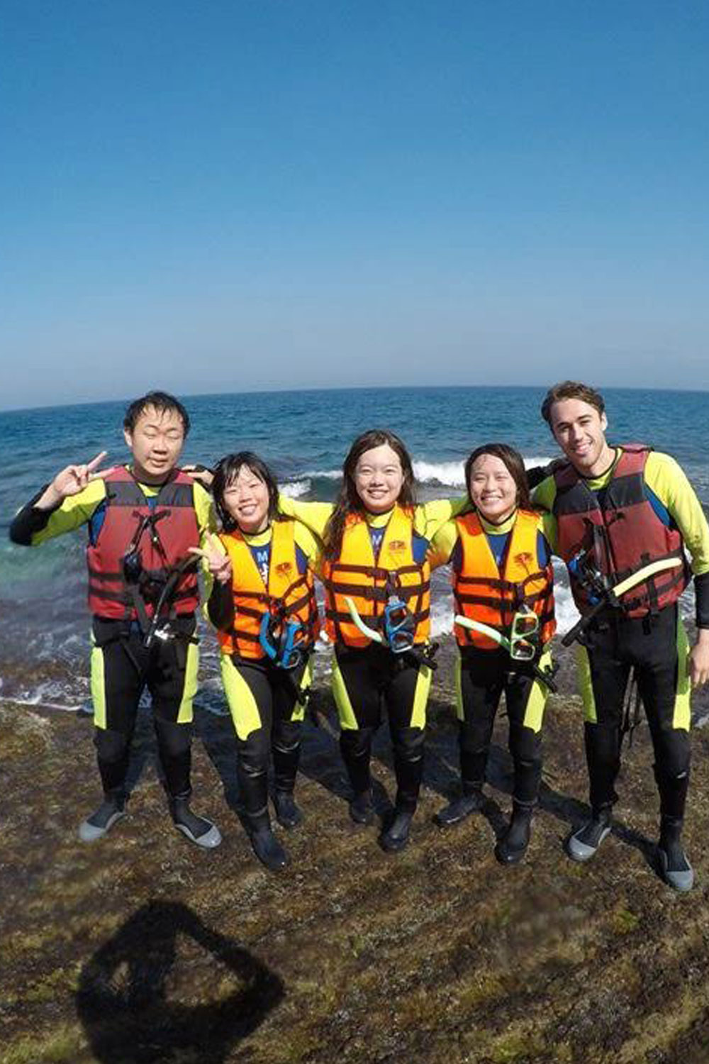 5 students wearing a life vest near the water.