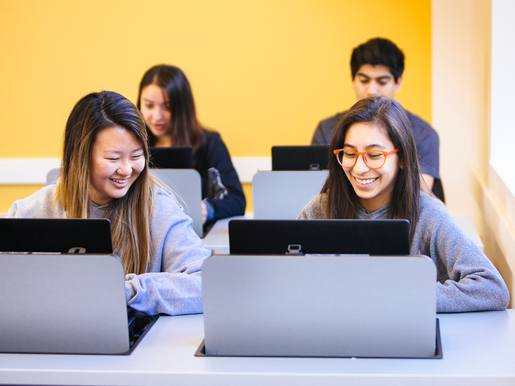 Four students on a computers in a computer room with yellow wall