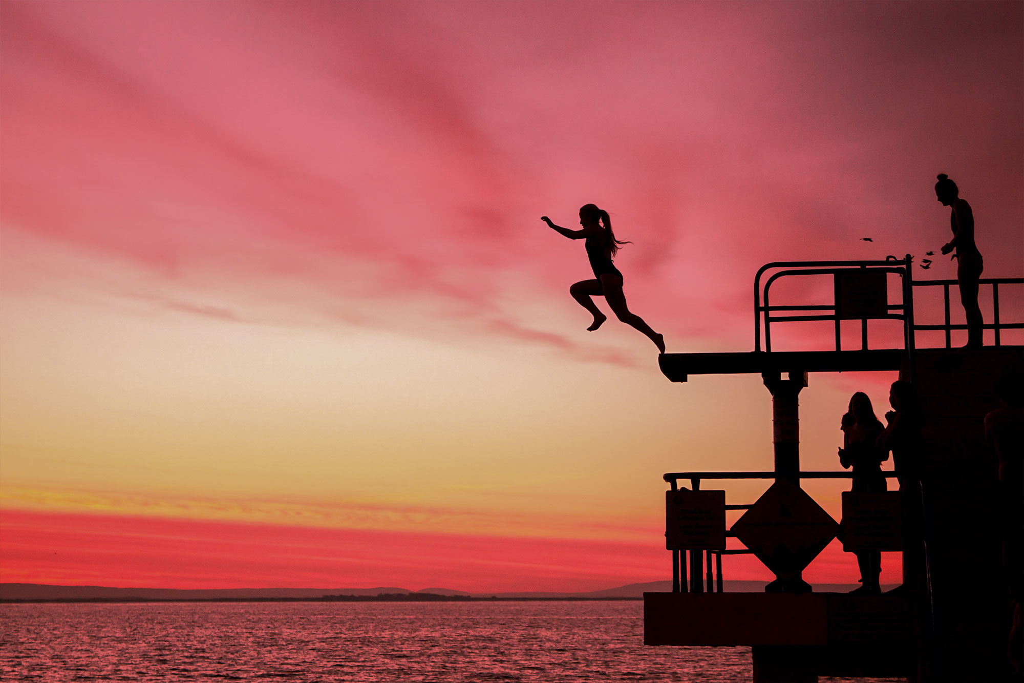 Person jumps off Blackrock Diving Tower at sunset, Galway, Ireland