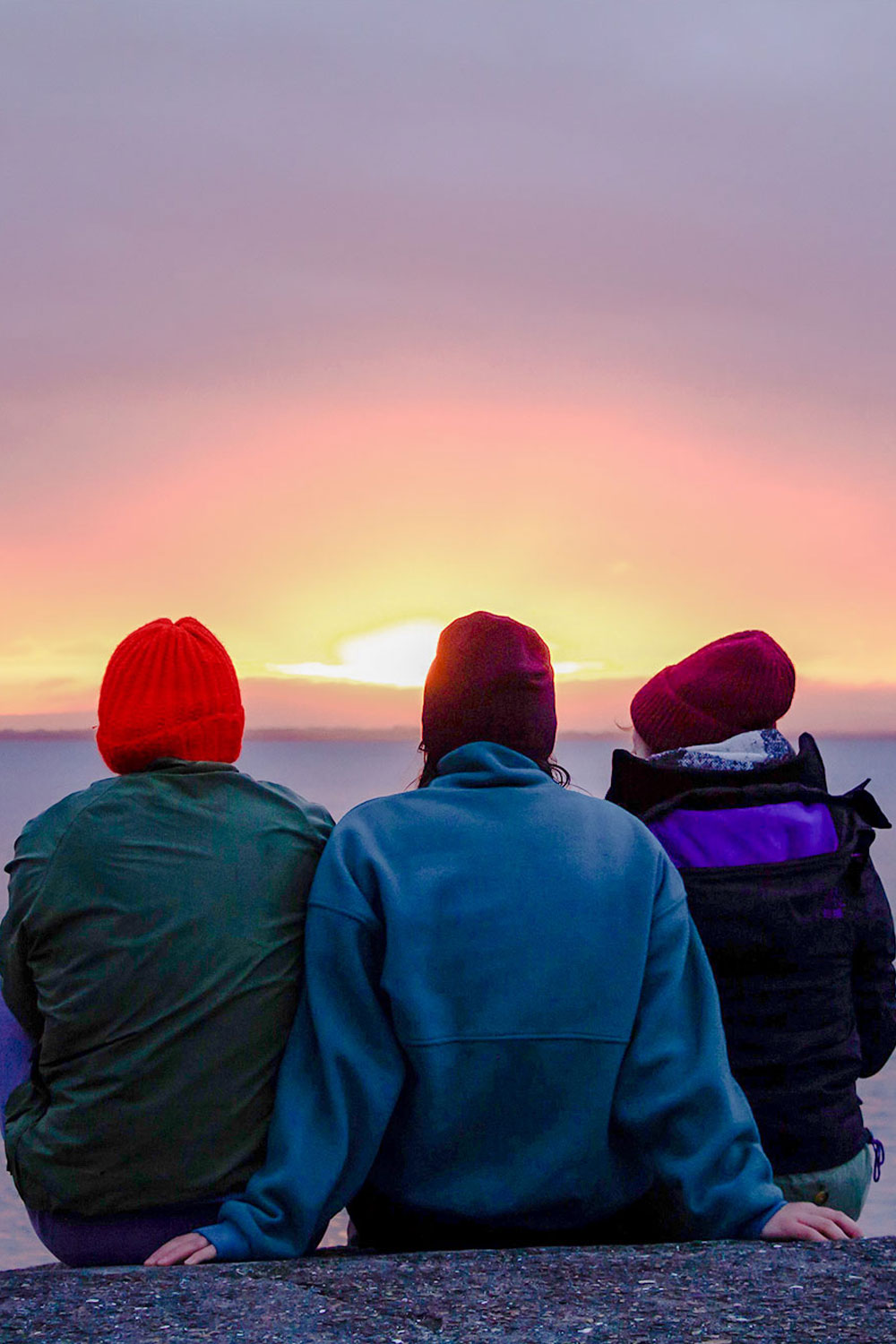 Three friends sitting watching the sunset on the Galway coast, Ireland.