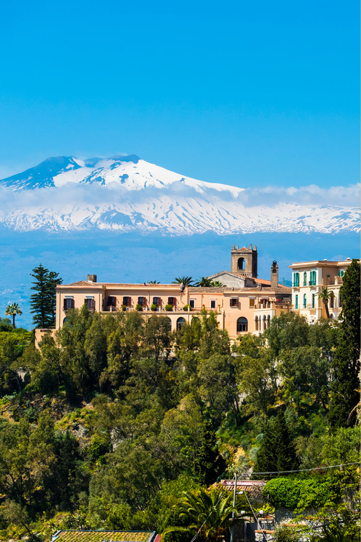 View overlooking terracotta hillside houses with snow-covered Mount Etna in the distance.