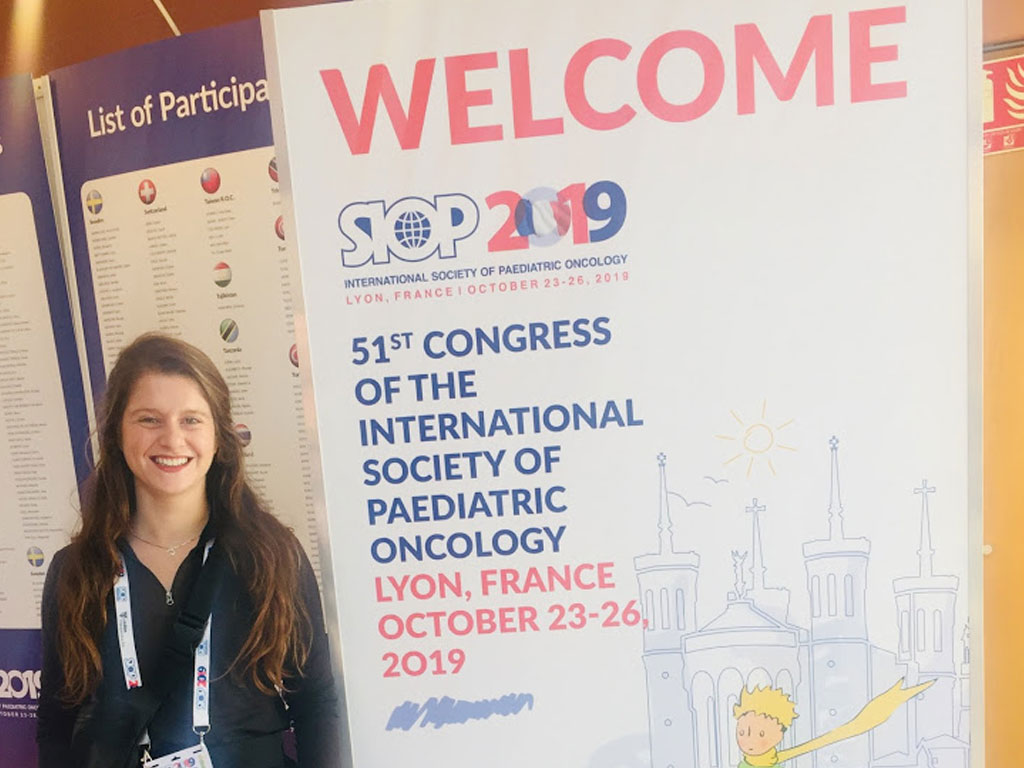 Sierra standing next to a poster during the 51st Congress of the International Society of Pediatric Oncology in Lyon France