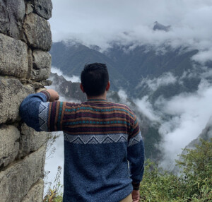 Ramil leaning against a stone wall looking out into nature.