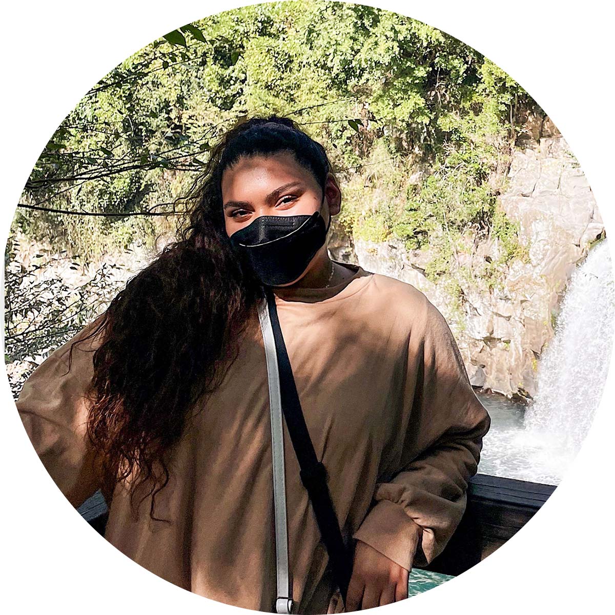 masked student posing fro camera in front of waterfall