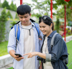 Two students chat about what is on a phone screen while exploring Thailand.