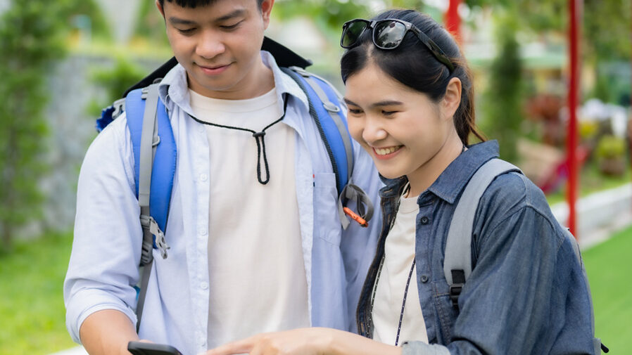 Two students chat about what is on a phone screen while exploring Thailand.