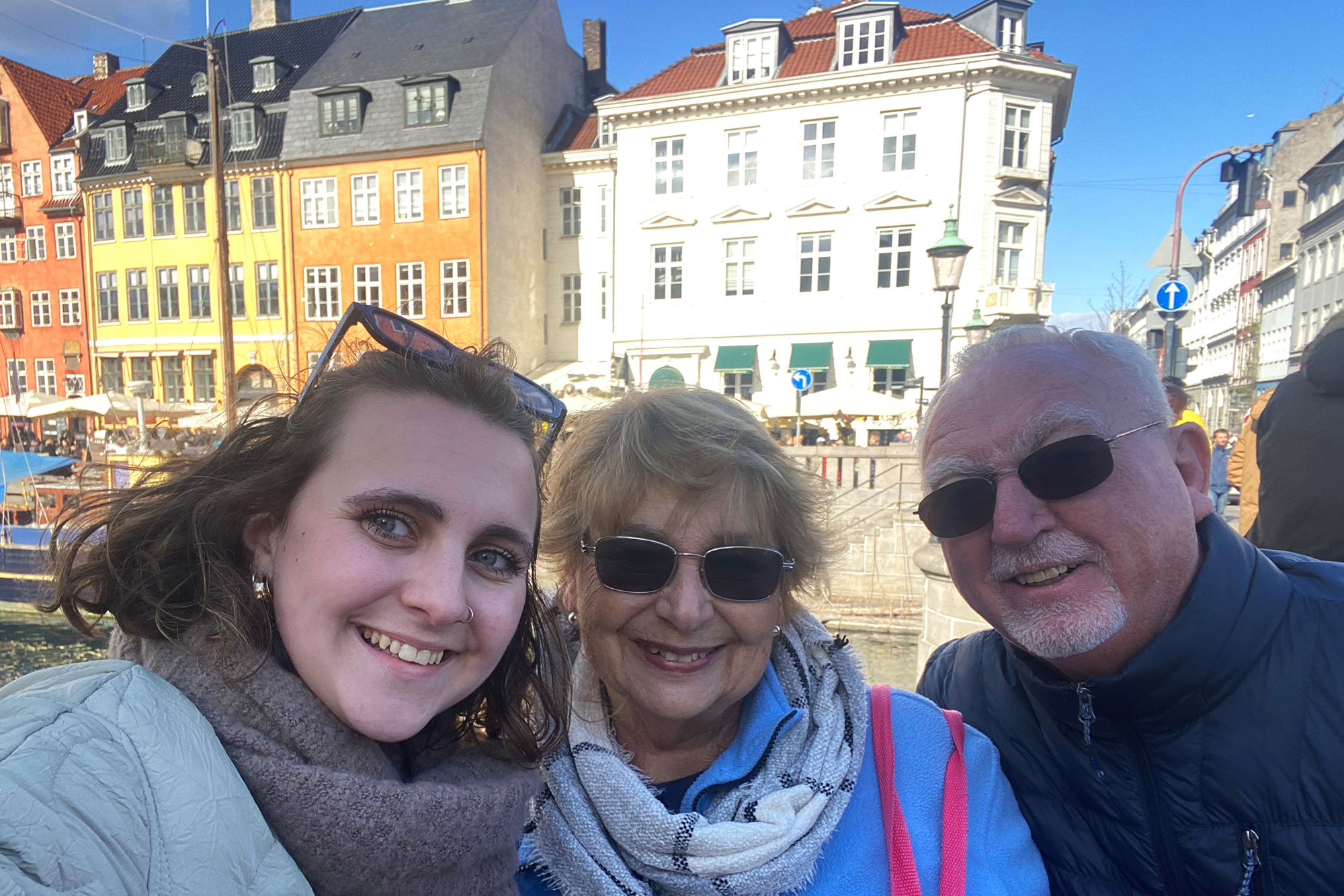 student with grandparents smiling in from the bright yellow, white, and orange houses of Nyhavn Canal, Copenhagen Denmark.
