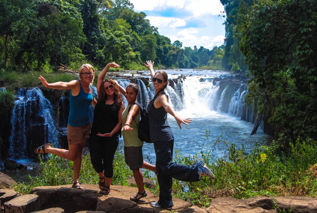 A group of female-presenting people pose for a photo in front of a waterfall on a sunny day in Taiwan.