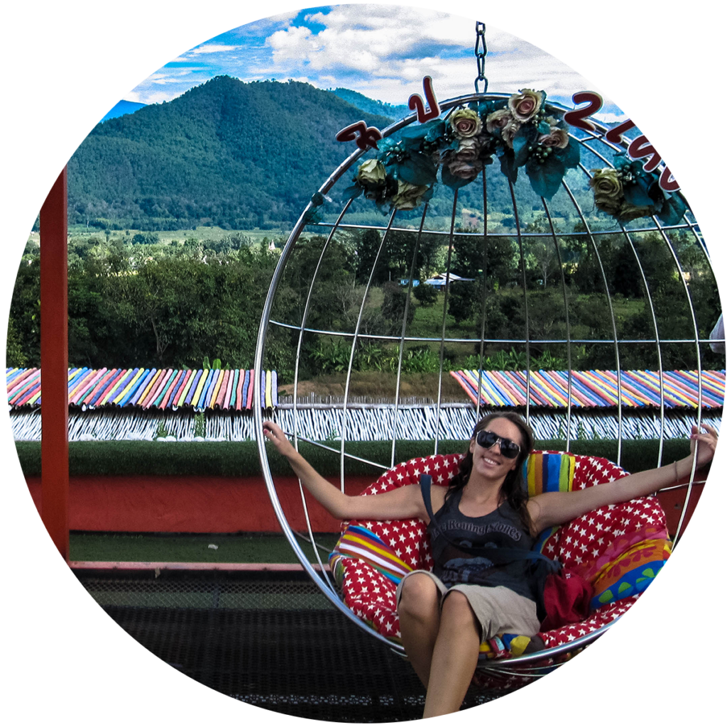 Kristin sits in a hammock seat and smiles, with a lush green mountain range in the background.