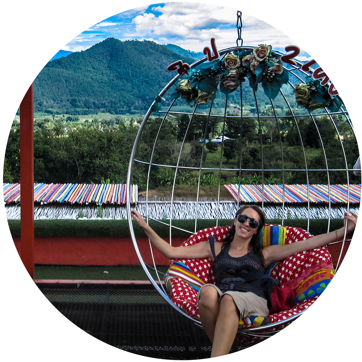 Kristin sits in a hammock seat and smiles, with a lush green mountain range in the background.
