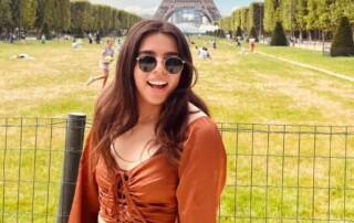 Student wearing sunglasses smiles while posing in front of the Eiffel Tower in Paris, France.