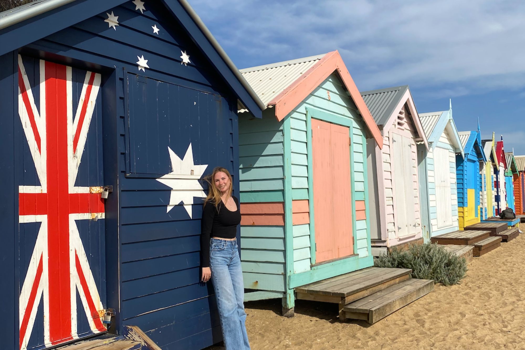 Student smiles while leaning against the Brighton Bathing Boxes in Melbourne, Australia