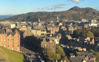 View of green rocky outcrop, Arthur's Seat, surrounded by the sandstone and redbrick city buildings of Edinburgh.