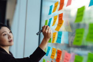 Young woman writing on sticky notes attached to the window. 