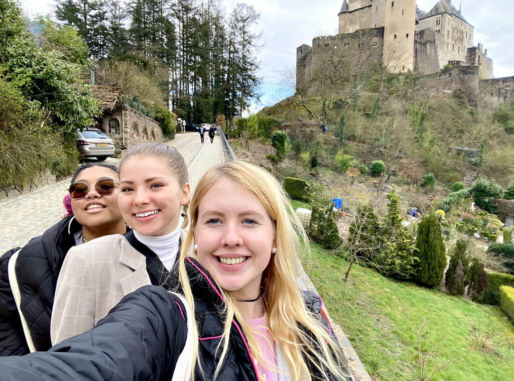 Three female college students taking a self-shot photo with castle in the background