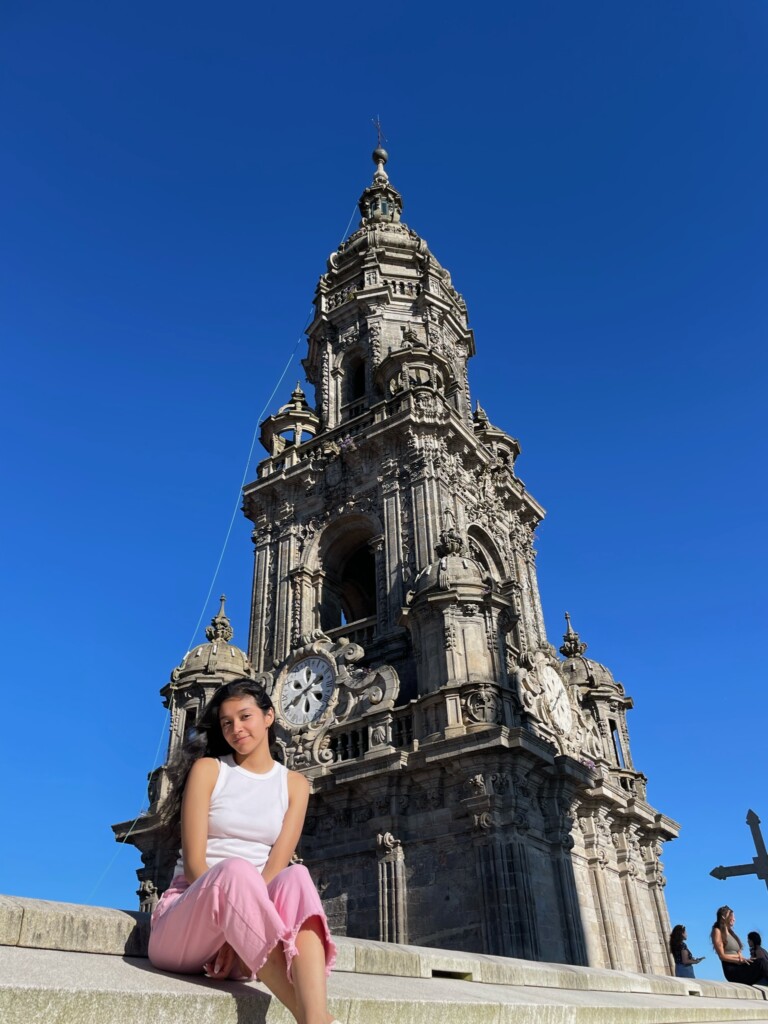 Female student sitting on steps smiling in front of church steeple.