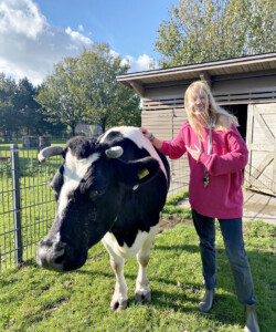 Blond female student positing for photo with a black and white cow