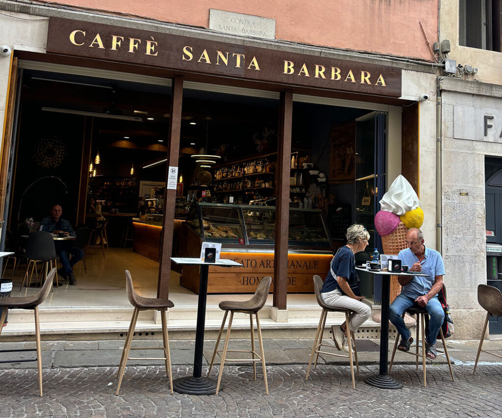 Two people in high bar-style table enjoying coffees in front of an Italian cafe called Cafe Santa Barbara