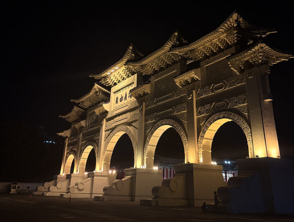Illuminated traditional Asian archway at night, featuring intricate designs and glowing warmly against a dark sky, evoking a serene and majestic atmosphere.