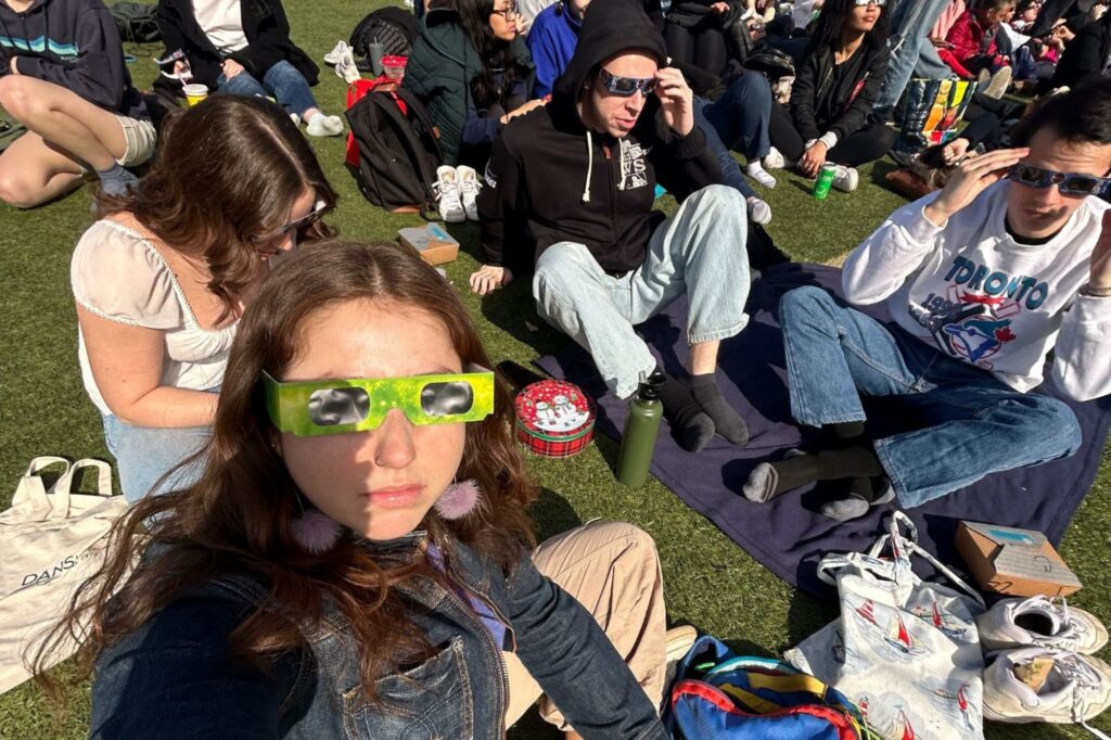 Lily in a park with protective glasses on, surrounded by other students