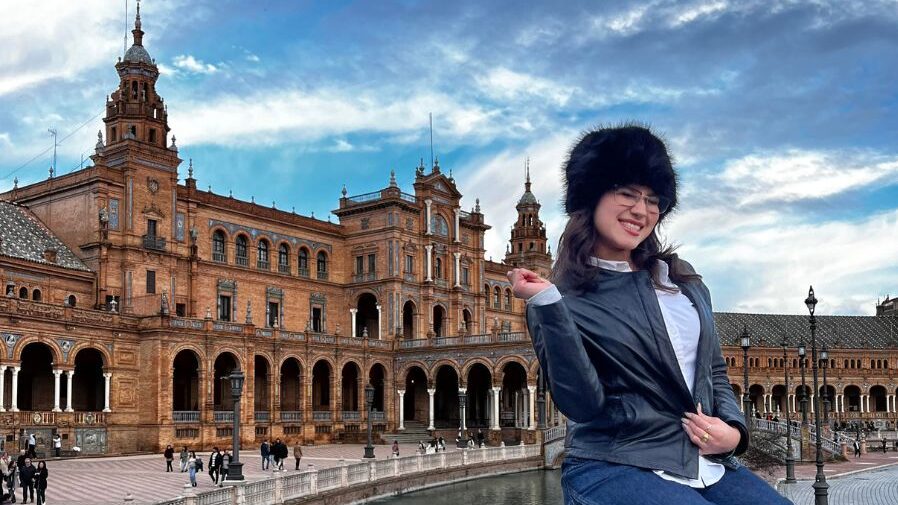 Terra Alvarez sitting on a wall with a hat, pointing behind her