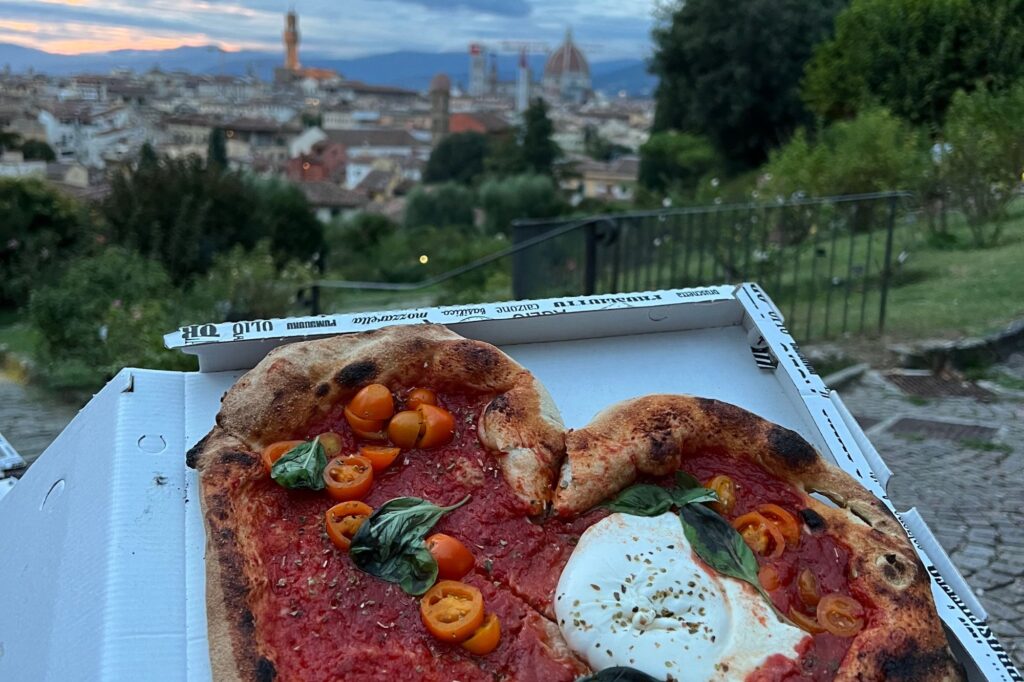 Heart-shaped pizza in a box over an Italian landscape